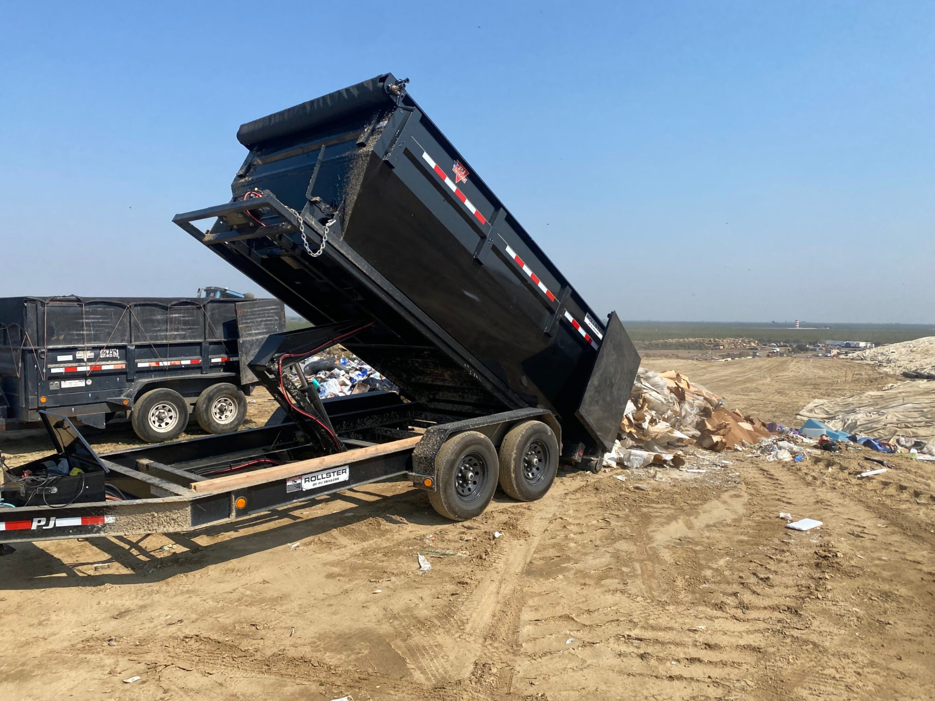 Black roll off dump trailer tipping debris at a landfill